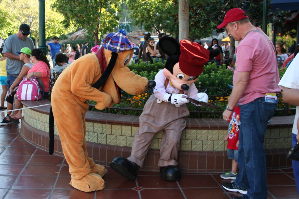 Mickey signs an autograph while faithful Pluto looks on