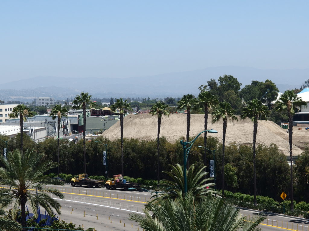 Construction vehicles parked on the street are dwarfed by the massive mound of dirt inside the project