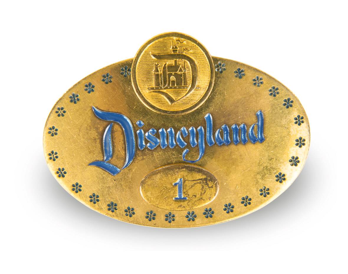 A photo depicts Disney Employee Badge Number 1, one of the historical artifacts that will be included in Disney100: The Exhibition. The badge has been photographed against a neutral white background. 