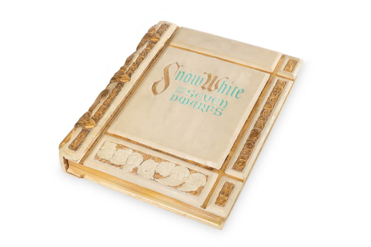 A photo depicts the prop storybook used in the opening of Snow White and the Seven Dwarfs, one of the historical artifacts that will be included in Disney100: The Exhibition. The storybook has been photographed against a neutral white background.